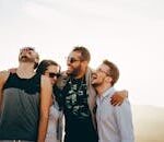 A group of young adults laughing and enjoying time together outdoors under the sun.